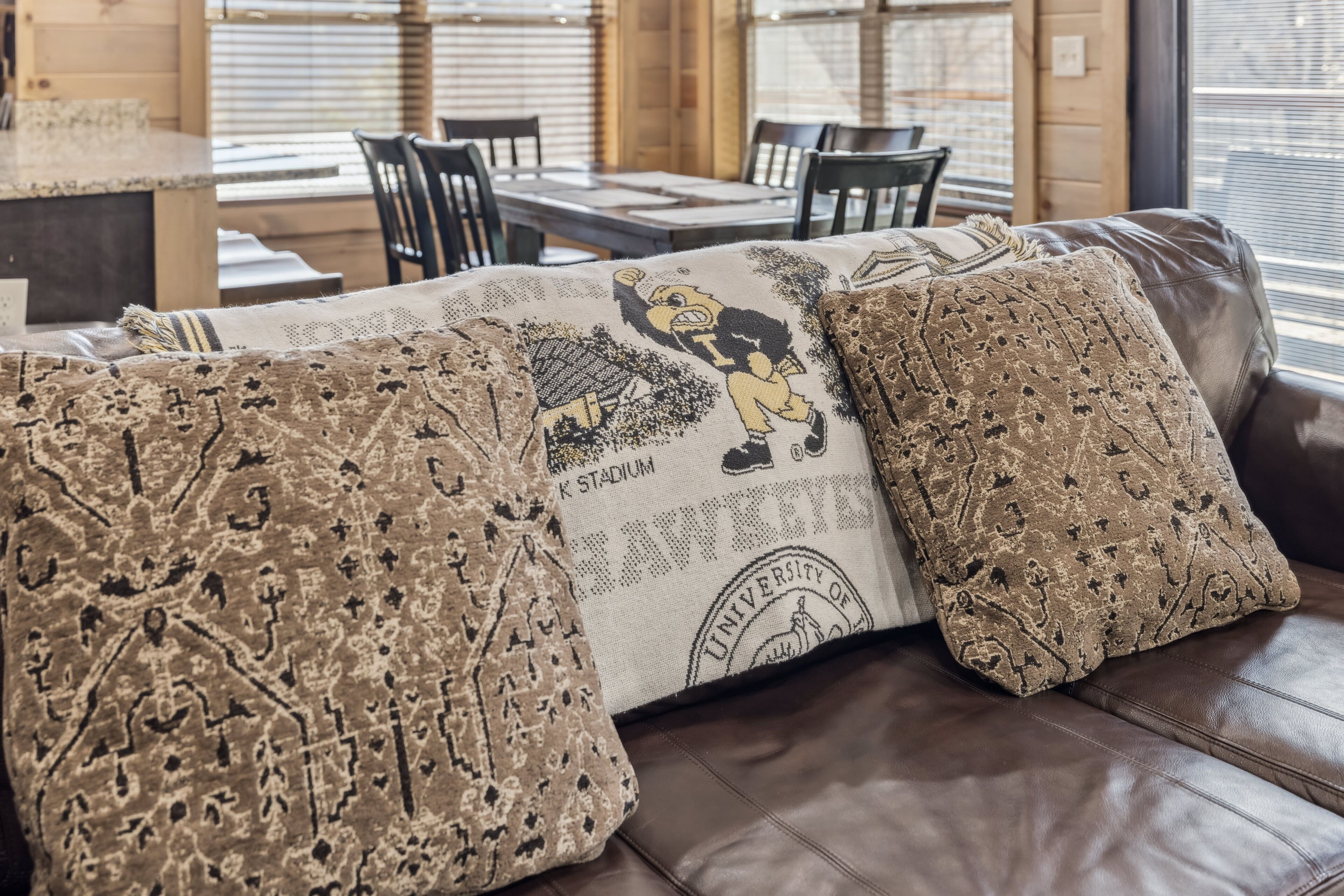 Un canapé en cuir avec des coussins à motifs et une table entourée de chaises, le tout sur un fond neutre.