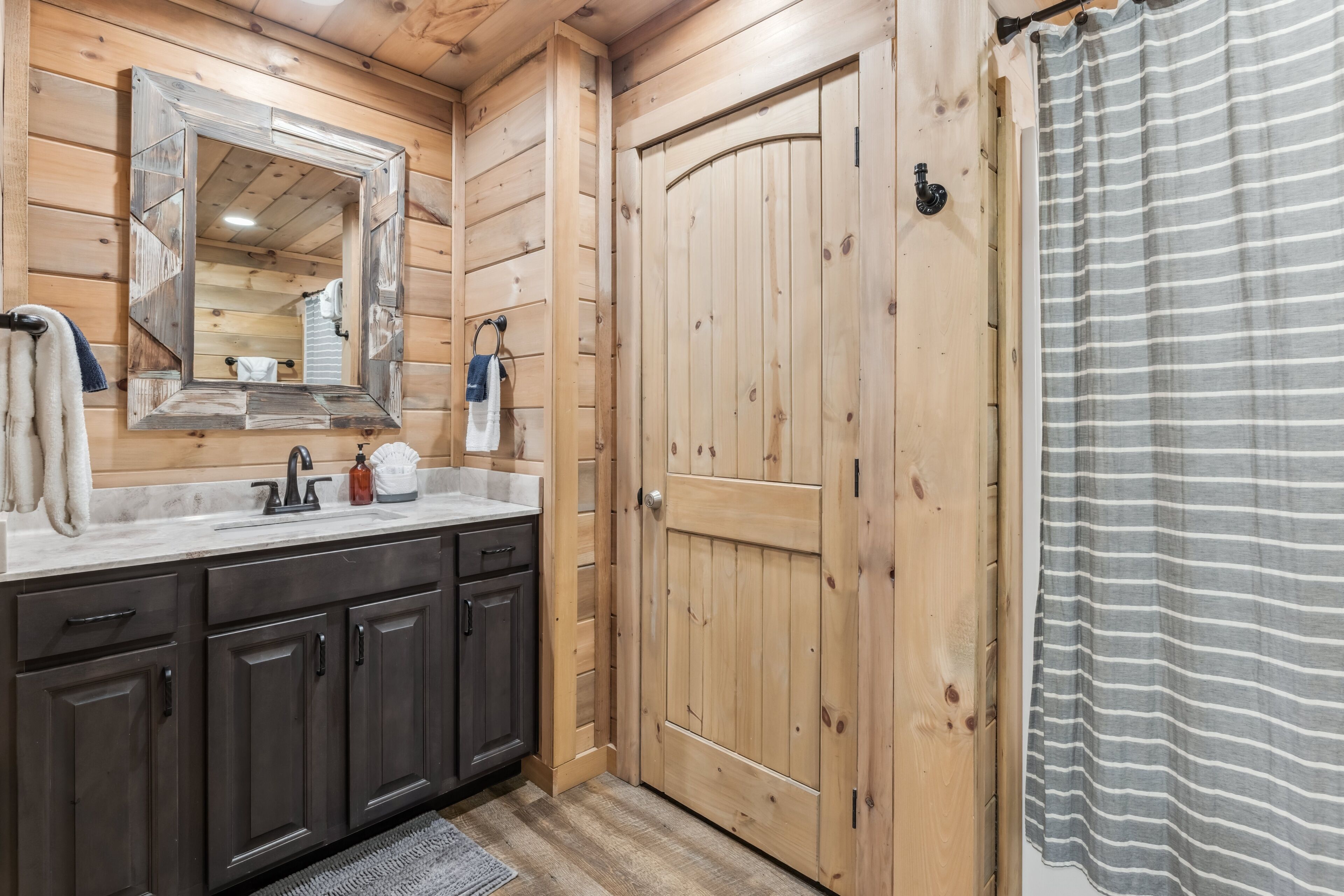A wooden bathroom with a sink, dark cabinets, a mirror, and a wooden door.