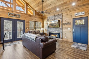 A cozy cabin interior with a leather sofa, a fireplace, and a 'Gather Here' sign. - Hawkeye Ridge 3 Bedroom Cabin by RedAwning (Sevierville)