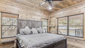 Un dormitorio con paneles de madera, una cama, ventanas amplias y un ventilador de techo.