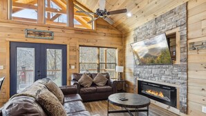 Un acogedor interior de cabaña con chimenea de piedra, sofás de cuero y un televisor grande montado en la pared.
