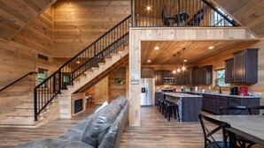 A cabin interior with a staircase, a sofa, a kitchen area, and a dining table.