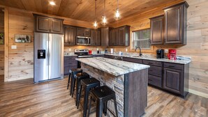 A modern kitchen with wooden paneling, stainless steel appliances, a granite countertop island, and bar stools.