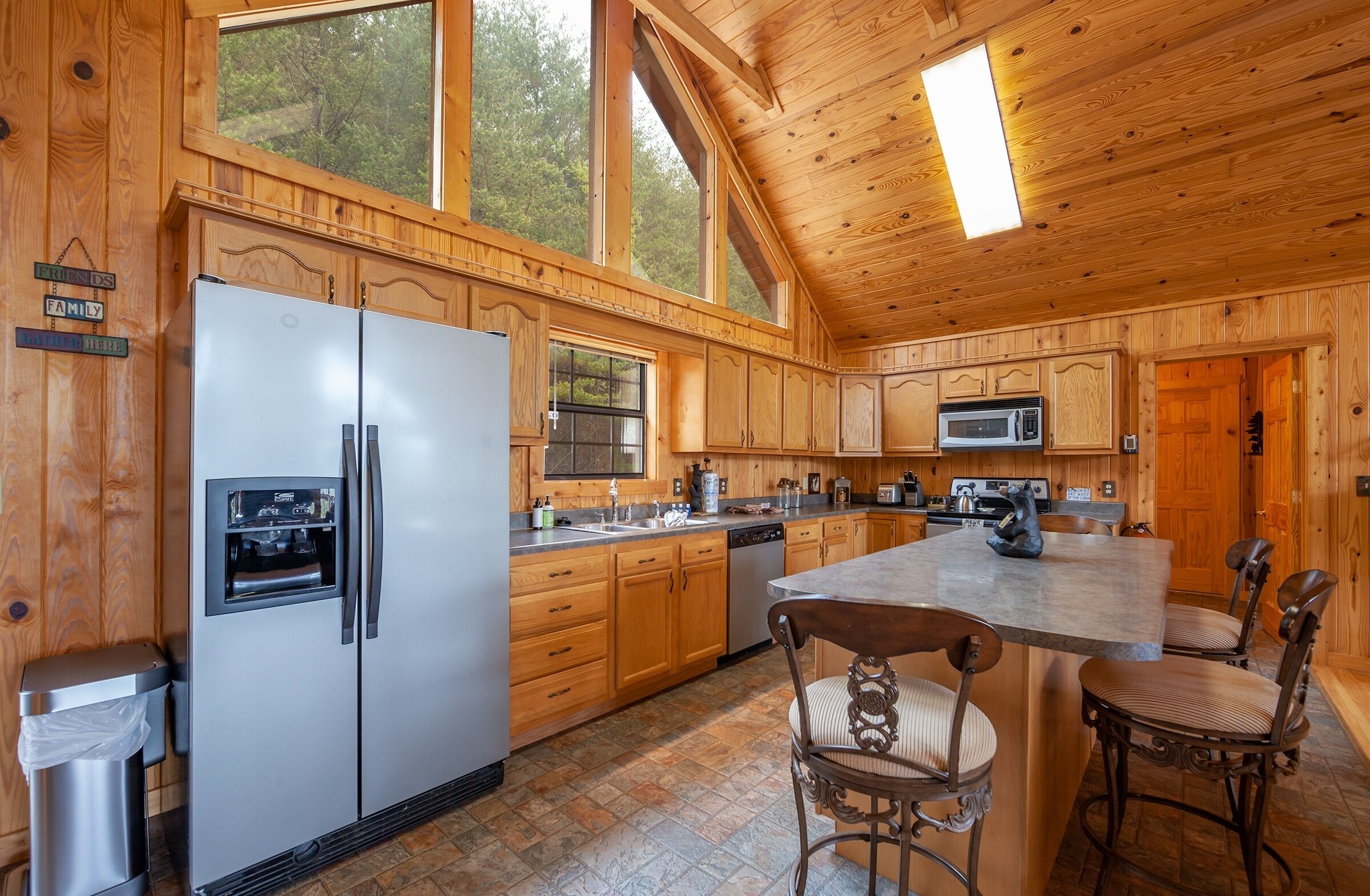 A spacious kitchen with wooden cabinets, a stainless steel refrigerator, a microwave, and a large island with chairs.