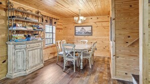 Ein Holzinterieur mit einem Esstisch und Stühlen, einem Schrank voller Brettspiele und einem gerahmten Bild an der Wand.