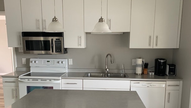 A modern kitchen with white cabinets, a central island with stools, a microwave, stove, sink, and a coffee maker. - Lake Front home near Sister Lakes area.  Pontoon rental available. (Decatur)