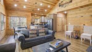 A cozy log cabin interior with a living room, dining area, kitchen, and a small dining table with chairs. - Brand New Freedom Cabin with Large Deck by RedAwning (Sevierville)