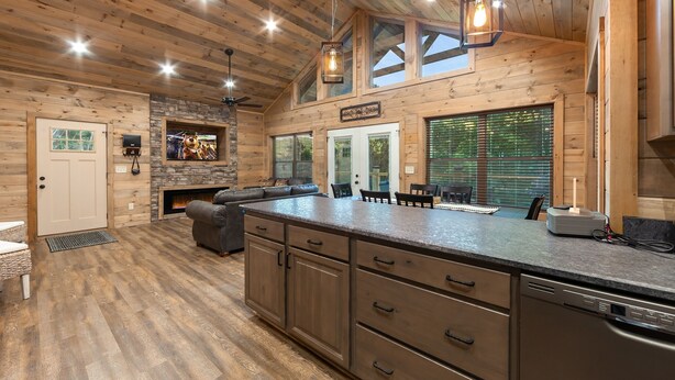 A spacious kitchen with a large island, wooden cabinets, and a stone fireplace. - Brand New Freedom Cabin with Large Deck by RedAwning (Sevierville)