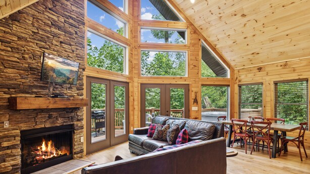 A spacious living area with a stone fireplace, a large couch, and a dining table with chairs. - Creekside Manor 3 Bedroom Cabin by RedAwning (Gatlinburg)