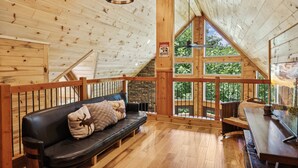 A wooden cabin interior with a black leather sofa, wooden dining table, and a stone fireplace. - Creekside Manor 3 Bedroom Cabin by RedAwning (Gatlinburg)