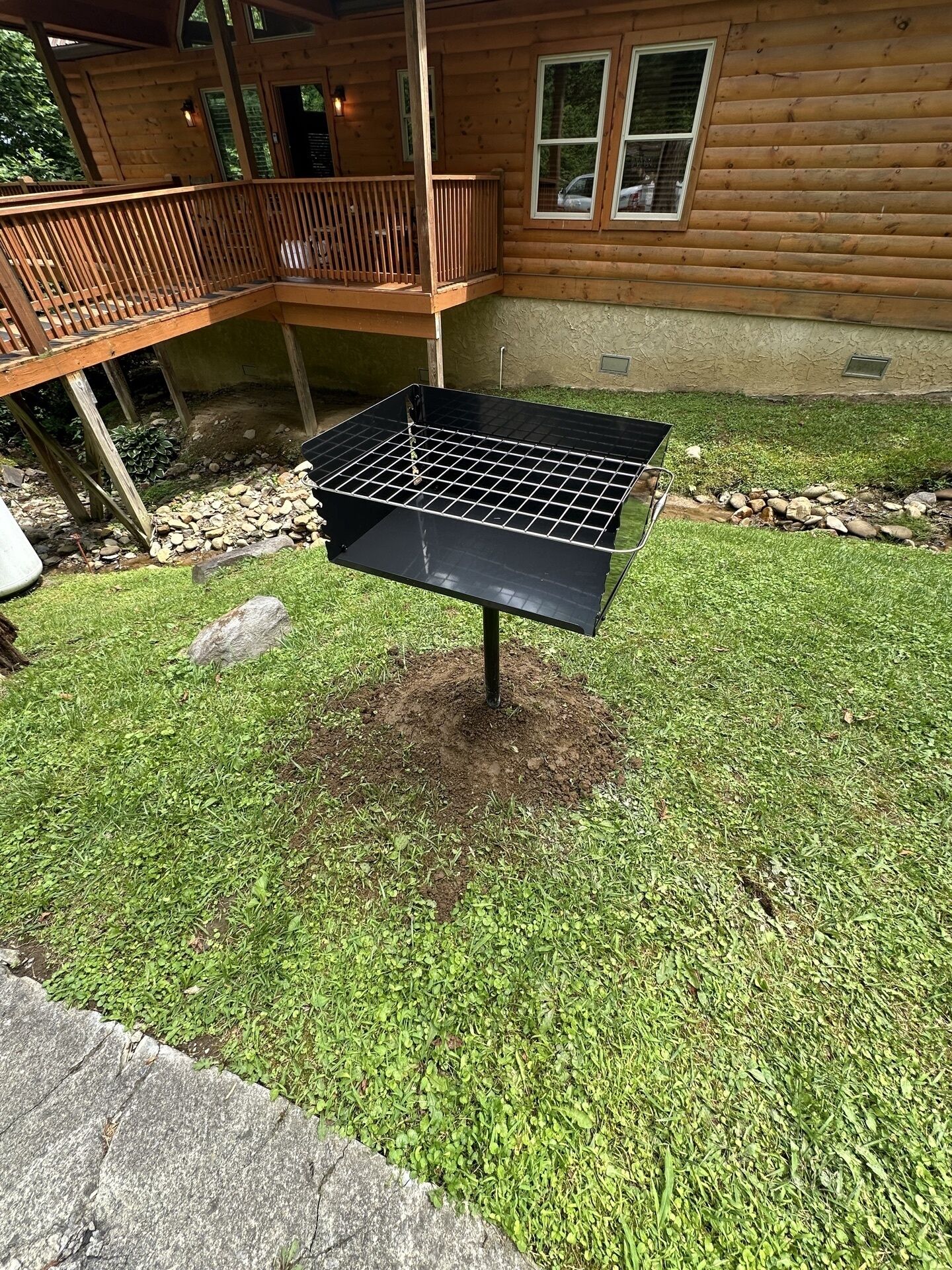 A barbecue grill in a backyard with a wooden deck and a house in the background.
