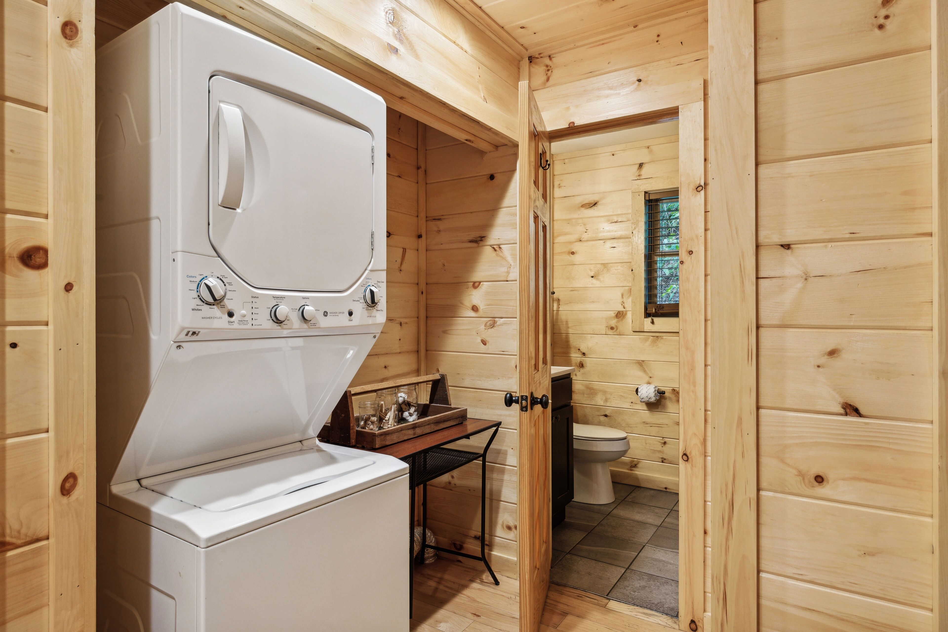 Una cabaña de madera pequeña y funcional con lavadora, una mesita y un inodoro.