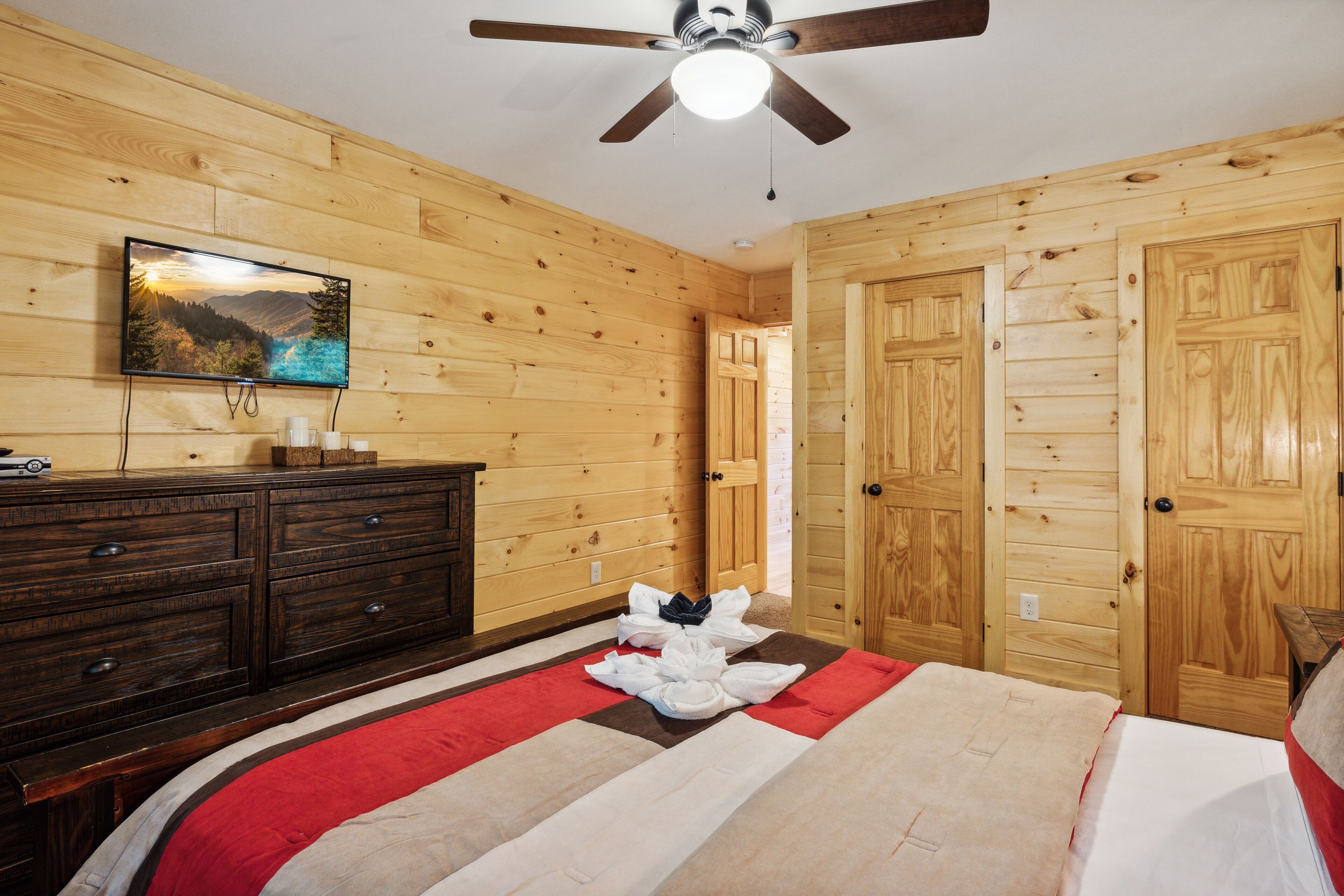 Una habitación con paneles de madera, una cama, un aparador, un televisor y un ventilador de techo.