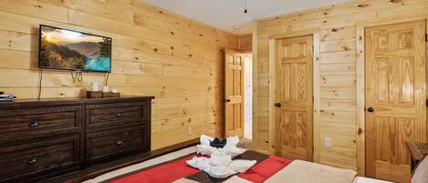 Una habitación con paneles de madera, una cama, un aparador, un televisor y un ventilador de techo.