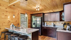 A kitchen with wooden walls, a marble island with stools, a refrigerator, and a coffee maker. - Creekside Manor 3 Bedroom Cabin by RedAwning (Gatlinburg)