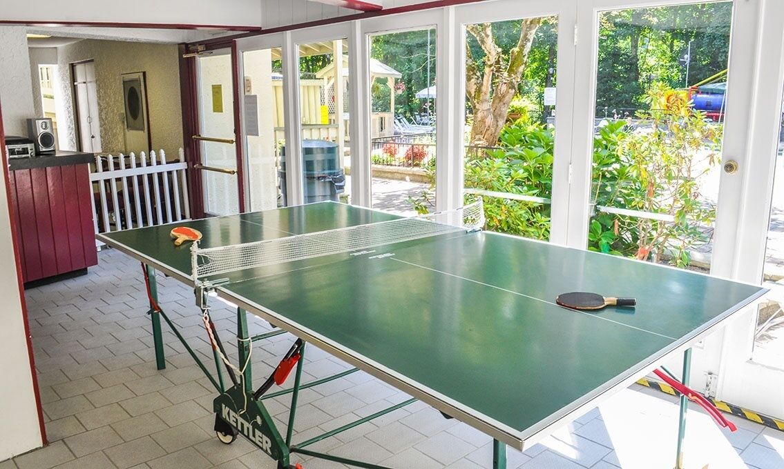 A ping pong table with paddles and a net in a room with large windows.