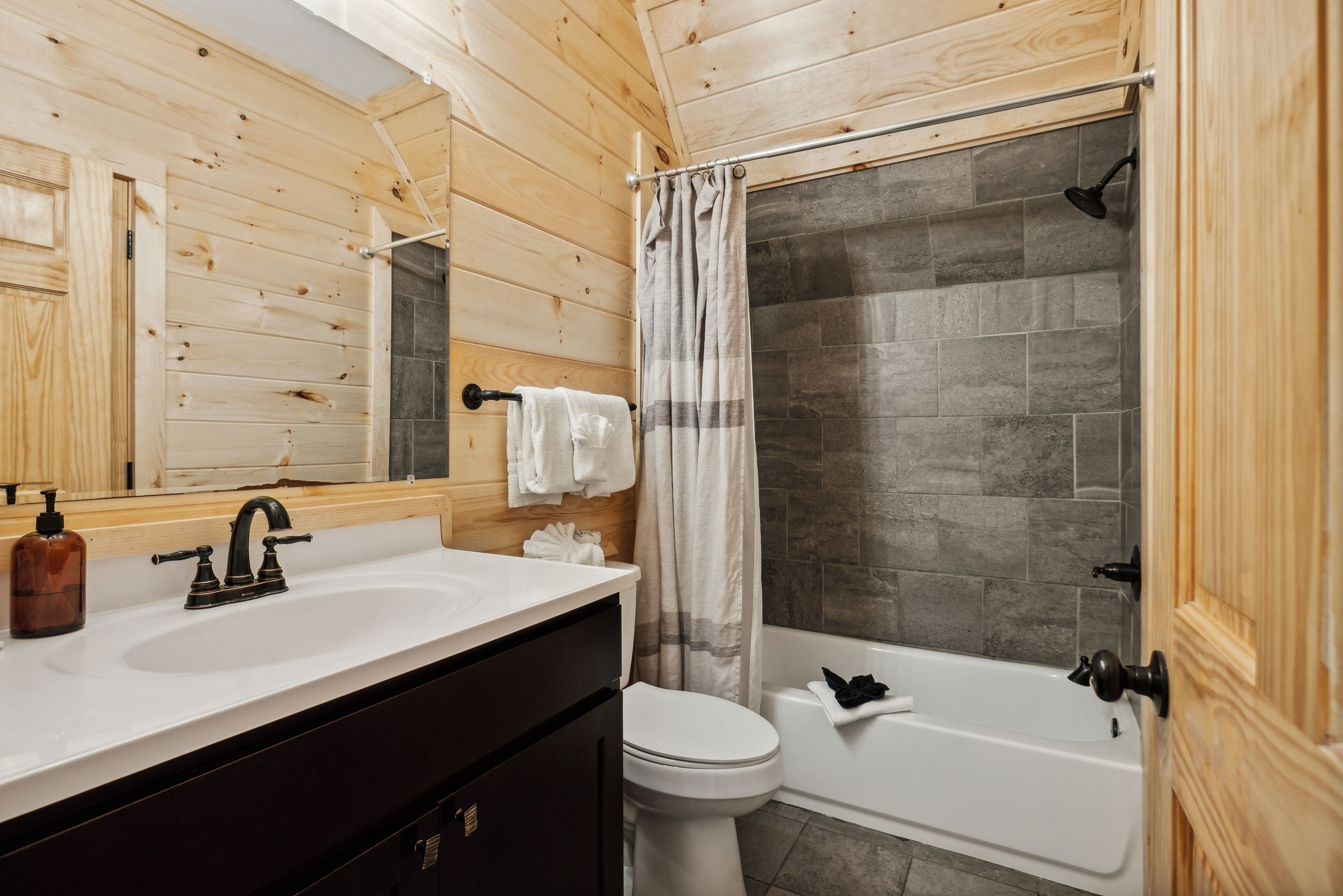 A bathroom with a wooden interior, a white sink, a toilet, and a bathtub.