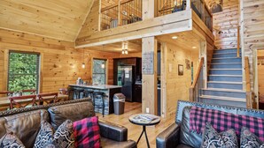 A spacious cabin interior with a dining area, kitchen, and a staircase leading to a loft. - Creekside Manor 3 Bedroom Cabin by RedAwning (Gatlinburg)