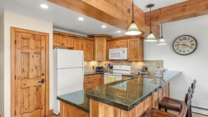 Una cocina con armarios de madera, un refrigerador blanco, un microondas, una estufa y un reloj en la pared.