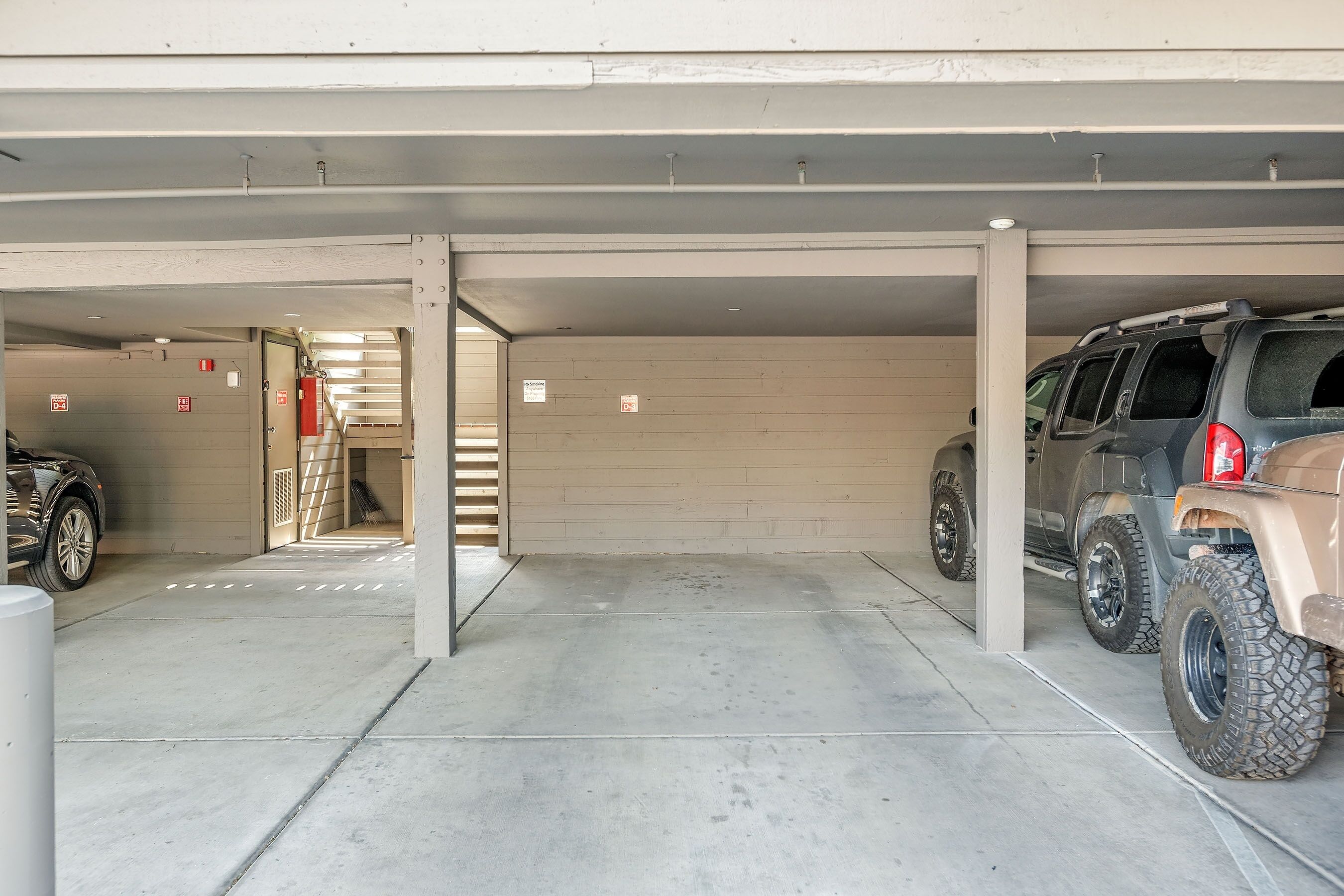 A parking garage with concrete floors and walls, a fire extinguisher mounted on the wall, and a vehicle parked in the right lane.