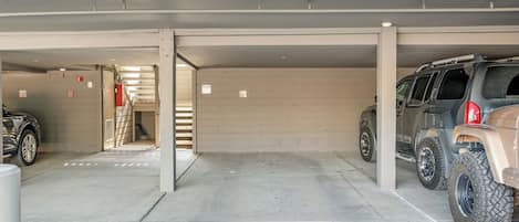 A parking garage with concrete floors and walls, a fire extinguisher mounted on the wall, and a vehicle parked in the right lane.