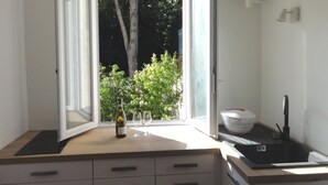 A kitchen with a window, a bottle of wine, two glasses, and a colander on the counter. - L'etoile Loire - Un Jardin en Ville ! (Saumur)