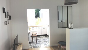 A modern kitchen with white cabinets, a black countertop, and a patterned floor. There is a dining area with a table and chairs, and a large mirror on the wall. - L'etoile Loire - Un Jardin en Ville ! (Saumur)