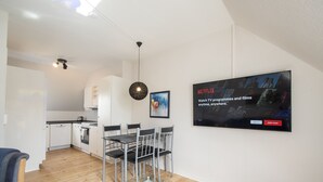 A modern living space with a kitchen, dining area, and a mounted TV displaying a Netflix advertisement. - City Town Square (Grasten)