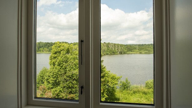 A window with a view of a lake surrounded by trees. - City Town Square (Grasten)