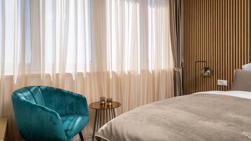 A bedroom with a bed, a blue chair, a small table with glasses, and sheer curtains.