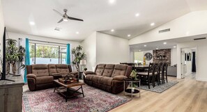 A modern living room with two brown sofas, a coffee table, and a dining area with a brick wall and wooden flooring.
