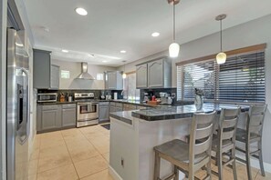 A modern kitchen with stainless steel appliances, a central island with bar stools, and a large window with blinds.
