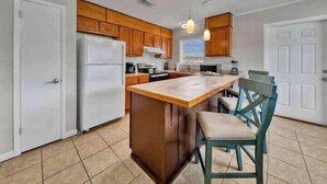 Una cocina con armarios de madera, un refrigerador blanco, una isla de madera y una silla.