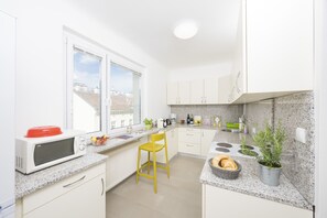 A modern kitchen with white cabinets, a red microwave, a yellow chair, a window with a view of buildings, and a potted plant. - Apartment cozy living in Vienna (Wien)