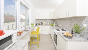 Una cocina moderna con armarios blancos, encimera de granito, microondas, fregadero y ventana con vistas a edificios.
