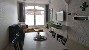 A modern living space with a dining area, a sofa, a TV mounted on a brick wall, and a potted plant. - Central Loft Apartment (Ueckermünde)