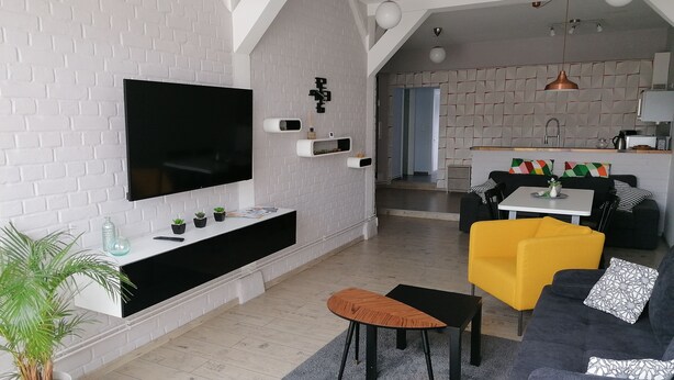 A modern living room with a flat-screen TV, a sofa, a coffee table, and a dining area with a table and chairs. - Central Loft Apartment (Ueckermünde)