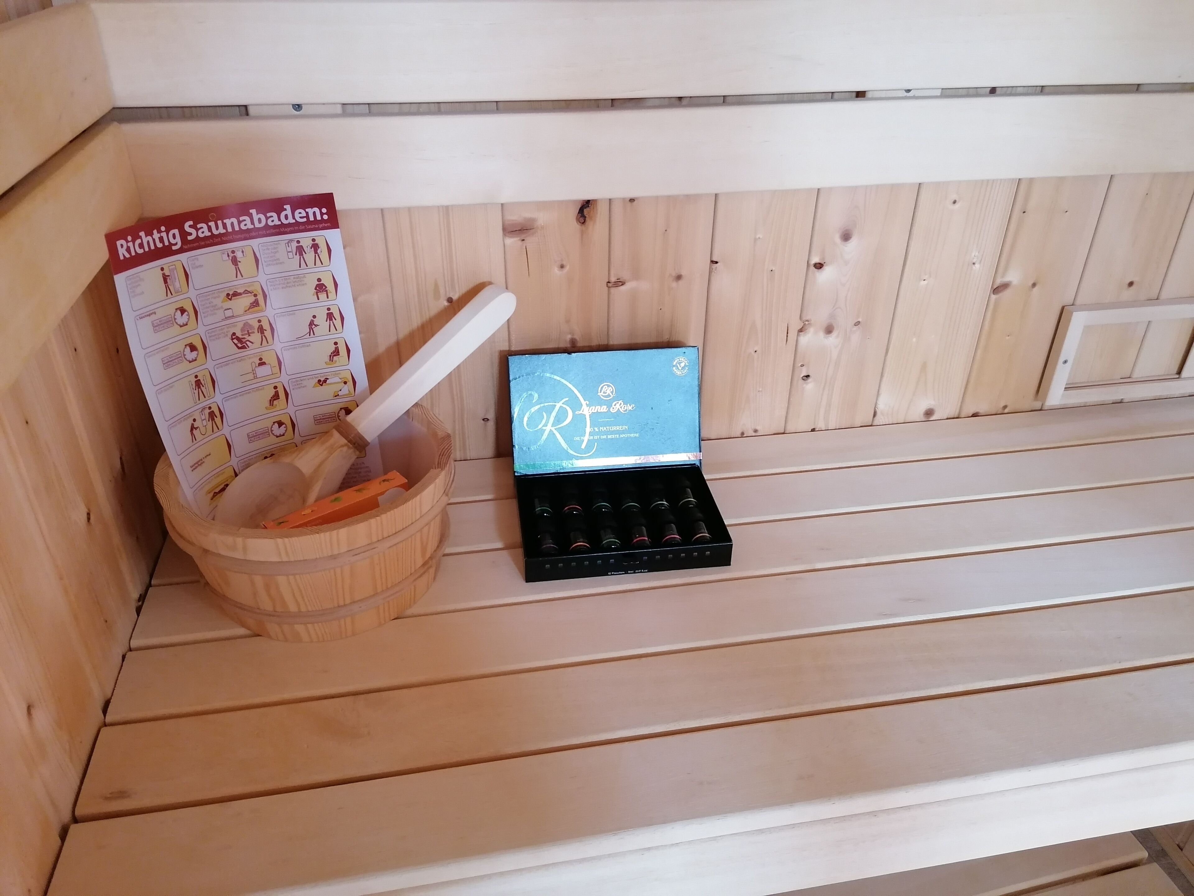 Ein Sauna-Bereich mit einer Holzbank, einem Holzeimer und einer Bürste sowie einer Produktbox.