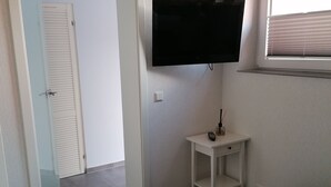 A hotel room with a bed, a TV mounted on the wall, a small table, and a window with blinds. - Central Loft Apartment (Ueckermünde)