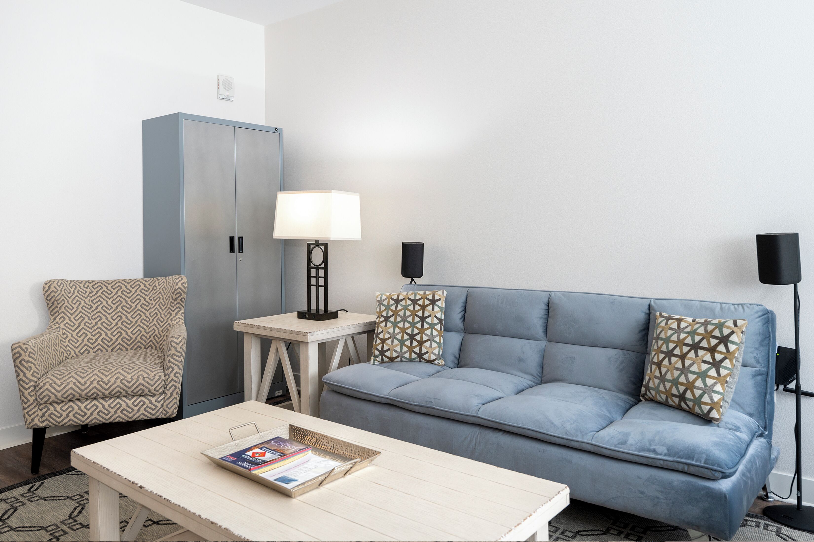 A living room with a sofa, armchair, coffee table, lamp, and a cabinet.