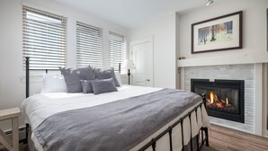 A bedroom with a large bed, a fireplace, and a framed picture on the wall. - Fraser Crossing 3518 remodeled studio gas fireplace and views (Winter Park)