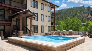 A rectangular pool with a brick border, a covered deck area, and a staircase leading to a second-floor balcony. - Fraser Crossing 3518 remodeled studio gas fireplace and views (Winter Park)