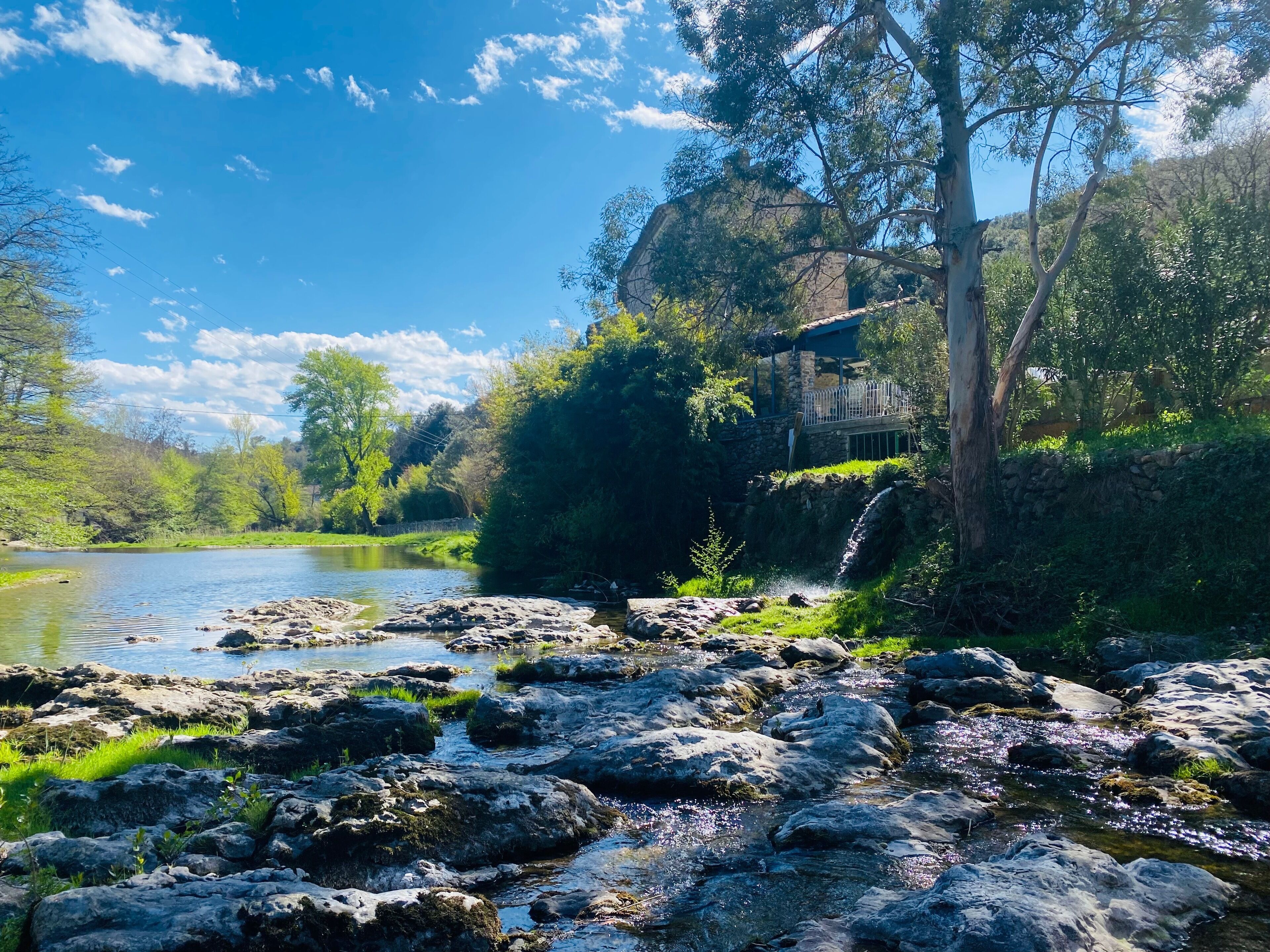 Un paisaje natural con un río, terreno rocoso y un edificio de piedra con un porche de madera.