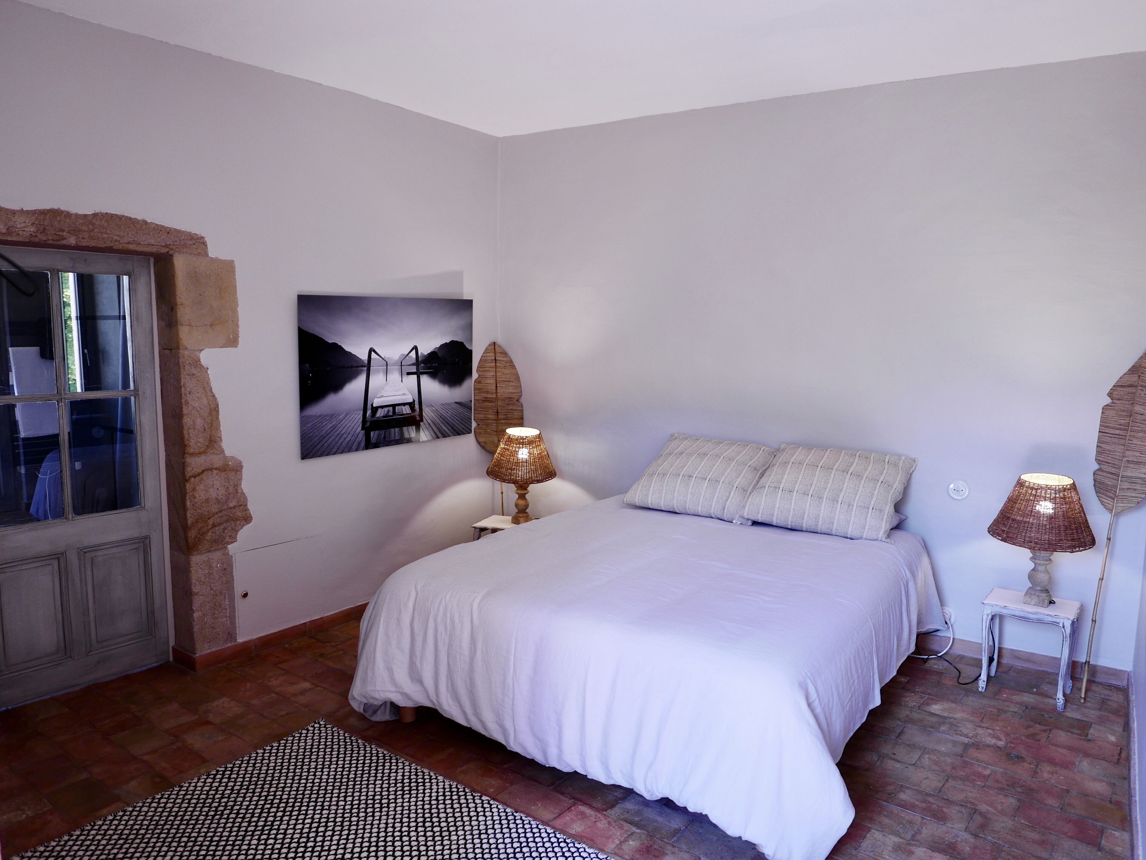 A bedroom with a bed, two bedside lamps, a wall-mounted picture, and a patterned rug.