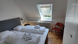 Une chambre à coucher avec un lit, des oreillers, une chaise, un radiateur et une fenêtre.