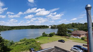 Une vue sur un lac, avec une vaste étendue d’eau, un bâtiment éloigné et une haute cheminée.