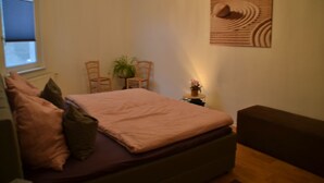 A bedroom with a bed, a nightstand, a chair, a potted plant, and a wall art piece. - Ferienwohnung mit Balkon im Zentrum von Eberwalde (Eberswalde)