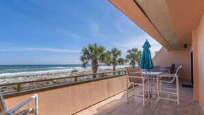Un balcon avec vue sur la plage et l’océan. On y trouve des chaises et une table, ainsi qu’un parasol bleu.