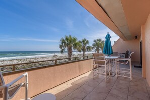 Ein Balkon mit Blick auf Strand und Meer. Es gibt Stühle und einen Tisch mit einem blauen Sonnenschirm.