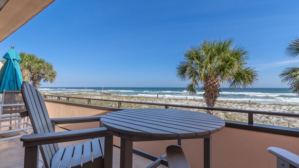 Un balcon avec une table et des chaises donnant sur une plage bordée de palmiers et où l’on peut admirer les vagues de l’océan.